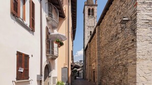 A narrow street with stone buildings, a visible bell tower, and a balcony with a hanging plant. - Il sogno di Elvira by Interhome (Domaso)