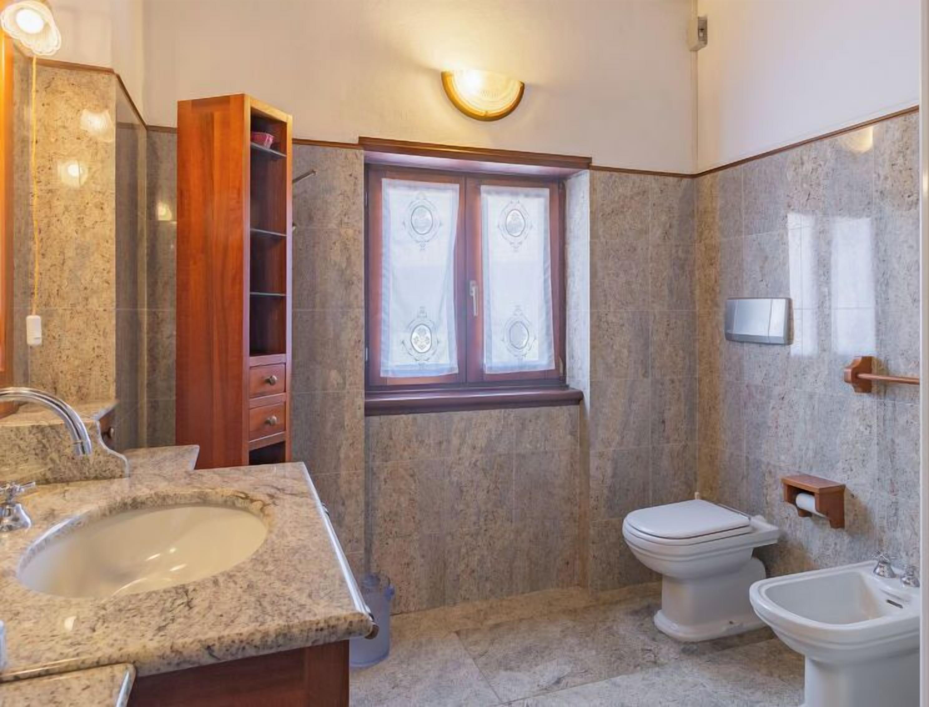 A bathroom with a granite sink, a toilet, a bidet, and a wooden cabinet.