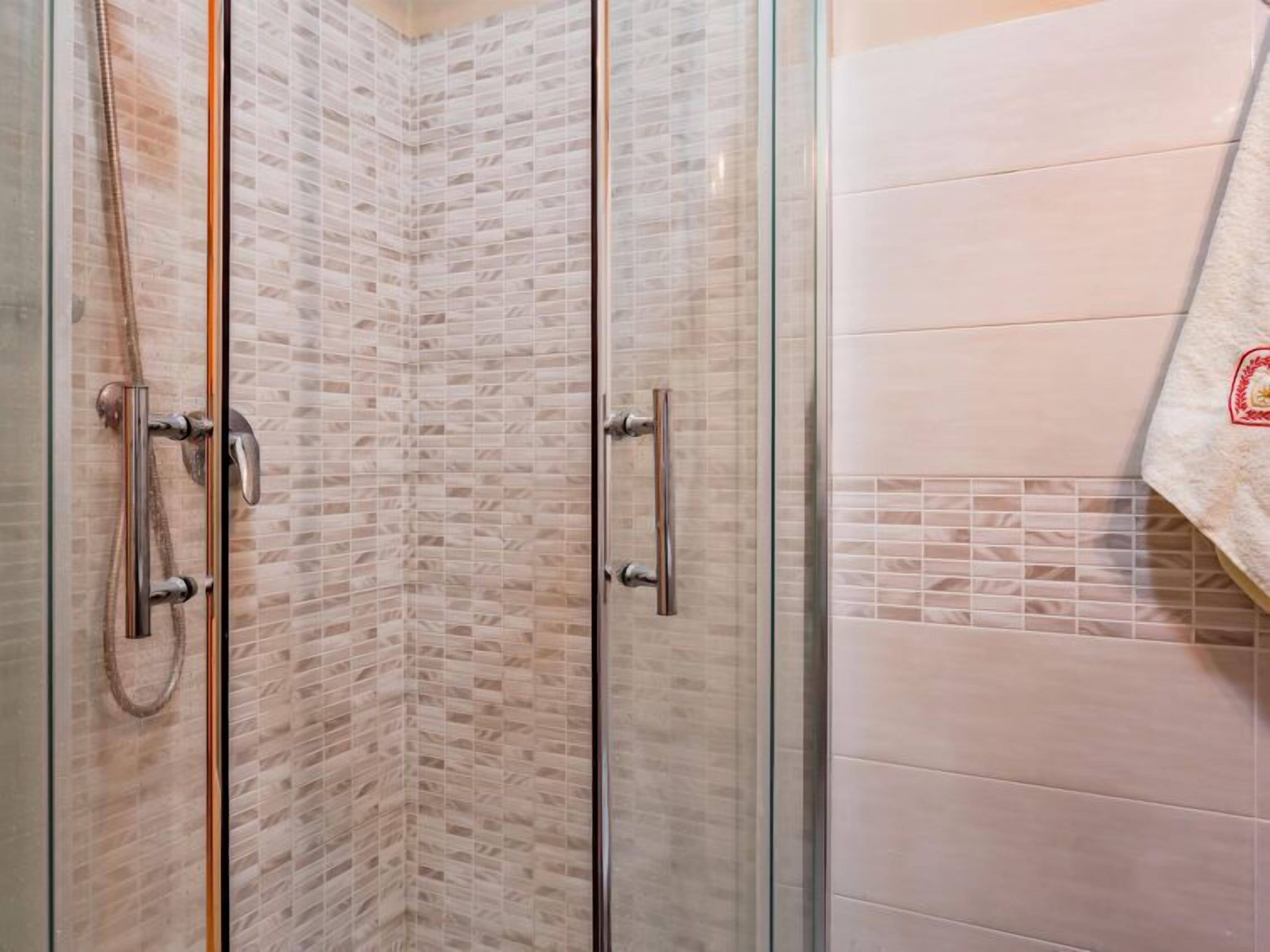 A corner shower with glass doors and a tiled wall.