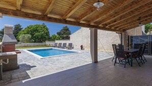 Un espacio al aire libre techado con piscina, sillas de descanso y una parrilla.