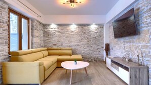 Una sala de estar moderna con una pared de piedra, un sofá modular amarillo, una mesa redonda y un televisor de pantalla plana montado en la pared.