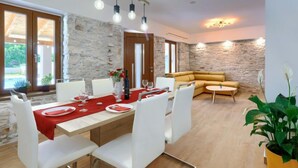 Un comedor con una pared de piedra, una mesa de madera preparada para cuatro personas y un sofá amarillo al fondo.