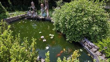 A pond with decorative statues and koi fish, surrounded by lush greenery.