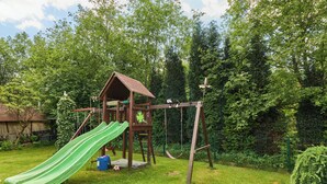 A wooden playhouse with a slide and swings in a grassy backyard.