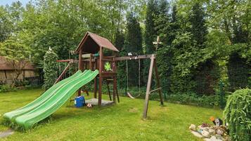 A wooden playhouse with a slide and swings in a grassy backyard.