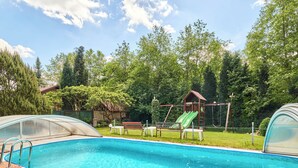A swimming pool with a slide, surrounded by a fenced area with benches and a covered seating area.