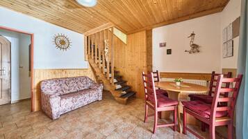 A wooden interior with a sofa, a dining table with chairs, a staircase, and a wall with framed certificates.