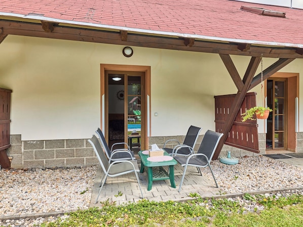 A patio area with a table and chairs, a wooden door, and a hanging plant. - Kačenka by Interhome (Desná v Jizerských horách)