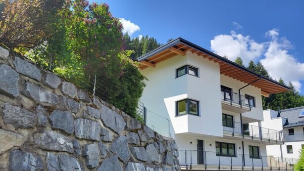 Ein modernes, mehrgeschossiges Gebäude mit einer Steinschmalseite, Balkonen und blauem Himmel.