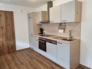 A modern kitchen with a wooden floor, white cabinets, a built-in oven, and a sink.