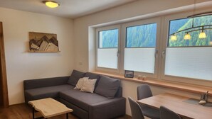 Ein modernes Wohnzimmer mit einem grauen Sofa, einem Holztisch und einem Essbereich mit Tisch und Stühlen.