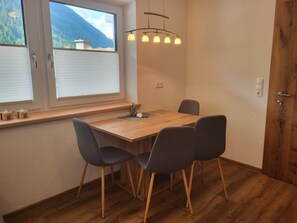 Une pièce avec une table en bois et quatre chaises, une fenêtre avec des stores, une porte en bois et un luminaire suspendu.