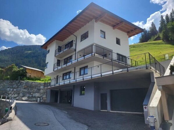 A multi-story building with balconies, a garage, and a stone wall.