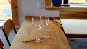 Una mesa de madera con dos copas de vino vacías, una silla y una ventana que da a vistas de árboles.