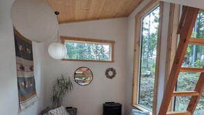 Una sala de estar acogedora con techo de madera, un sofá, una mesa de centro, una estantería y un ventanal con vistas a árboles.