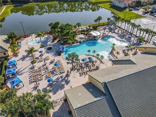 Relax by the resort's large, curved pool surrounded by lounge chairs and umbrellas, with a tranquil water feature nearby.