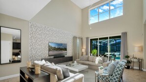 Ein geräumiges Wohnzimmer mit großem Fernseher, bequemen Sitzgelegenheiten, einem Couchtisch und Blick ins Freie.