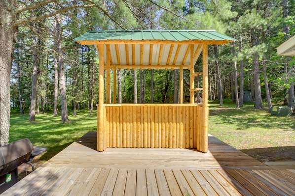 Un gazebo in legno con tetto verde, immerso in una zona boschiva.