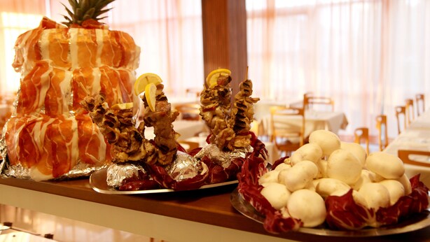 A buffet with various food items including a pineapple, skewers, and a plate of white round items. - Hotel Alfa (Rimini)