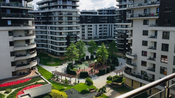 Een hoog appartementencomplex met meerdere balkons, een binnentuin met beplanting en een speeltuin.