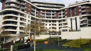 Een meerlaags woongebouw met balkons, een speeltuin en een voetpad.