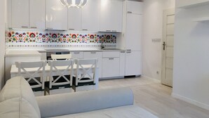 Een moderne keuken met witte kasten, een kleurrijke achterwand en een eethoek met witte stoelen en een tafel.