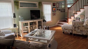 A living room with a television, a coffee table, a sofa, and a patterned armchair. - Beautiful old style beach cottage 
Walk to beach/ restaurants 
Center of town (Branford)