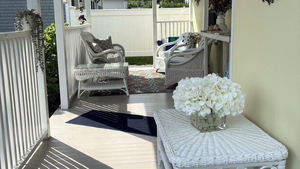 A covered porch with wicker furniture, a small table with flowers, and a white railing. - Beautiful old style beach cottage 
Walk to beach/ restaurants 
Center of town (Branford)