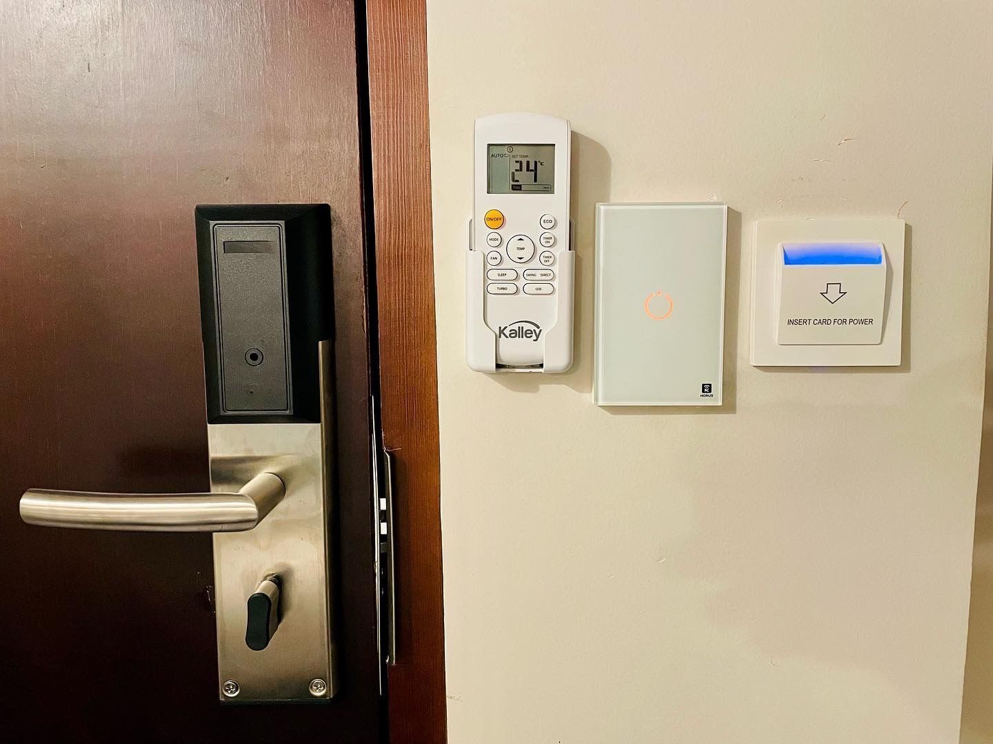 A modern door with a card reader, a remote control, and a power outlet on the wall.