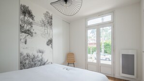 A bedroom with a large bed, a wall-mounted artwork, a wicker chair, and a view of the outside through a door. - A bright cocoon for a pleasant stay in Arcachon (Arcachon)