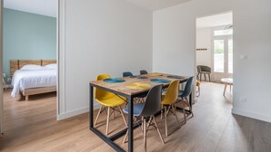 A modern room with a wooden floor, a bed with white bedding, a dining table with colorful chairs, and a large window. - A bright cocoon for a pleasant stay in Arcachon (Arcachon)