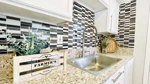 Una cocina con salpicadero a cuadros, un lavamanos de acero inoxidable y un letrero de madera que dice "FARMER'S MARKET".