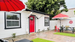 Una casa blanca con puerta roja, un patio con sombrilla roja y una pequeña mesa con sillas.