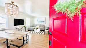 Una sala de estar moderna con una puerta roja, un televisor de pantalla plana, un sofá gris y un comedor con mesa de madera.
