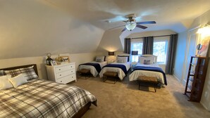 Quarto com duas camas, um ventilador de teto, cômoda e janela com cortinas.