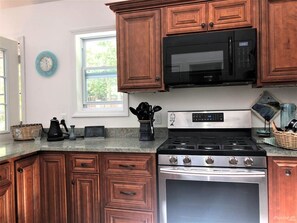 A kitchen with wooden cabinets, a stainless steel stove, a microwave, and a clock on the wall.