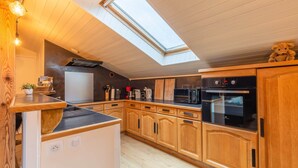 Eine Küche mit Holzausbau, einer Mikrowelle, einem Backofen und einem Gasherd. Über der Küche befindet sich ein Oberlicht.