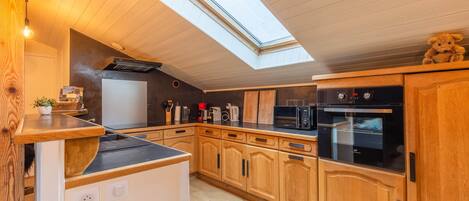 A kitchen with wooden cabinets, a microwave, an oven, and a gas stove. There is a skylight above the kitchen.