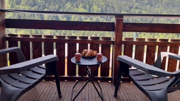 Ein Balkon mit Tisch und Stühlen mit Blick auf einen bewaldeten Berg.