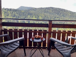 Un balcón con mesa y sillas, con vista a una montaña boscosa.
