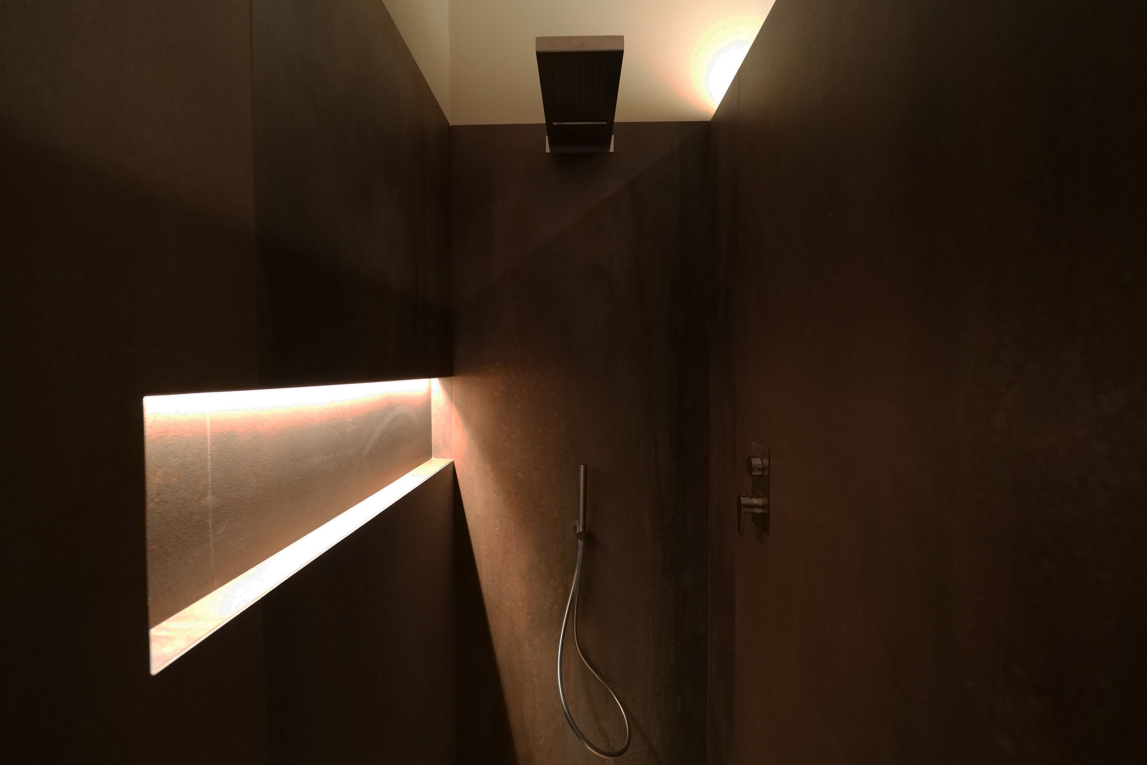 Un baño moderno con un diseño elegante, que incluye un cabezal de ducha empotrado y un panel iluminado.