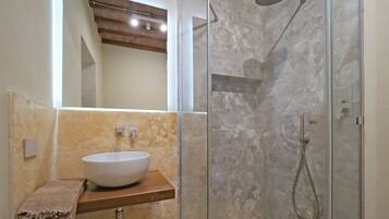 Un baño con un lavabo blanco, una cabina de ducha de vidrio y una encimera de madera.