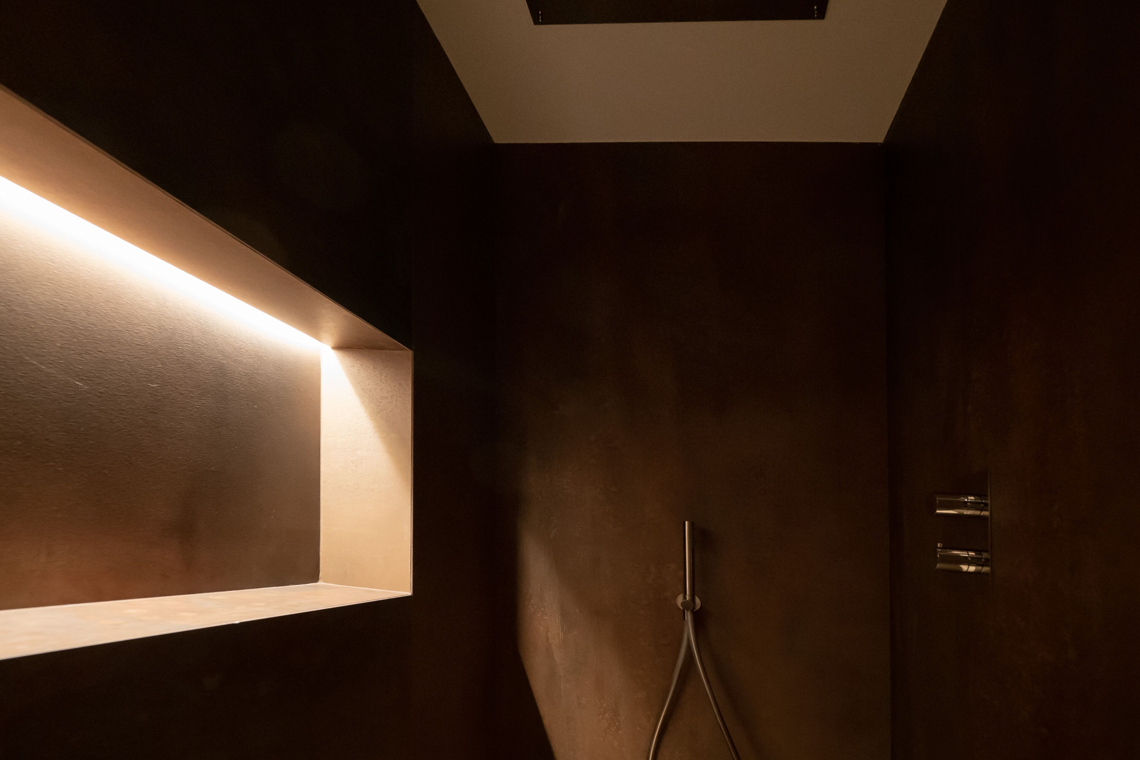 Un baño de color oscuro con una lámpara de pared y una zona de ducha.