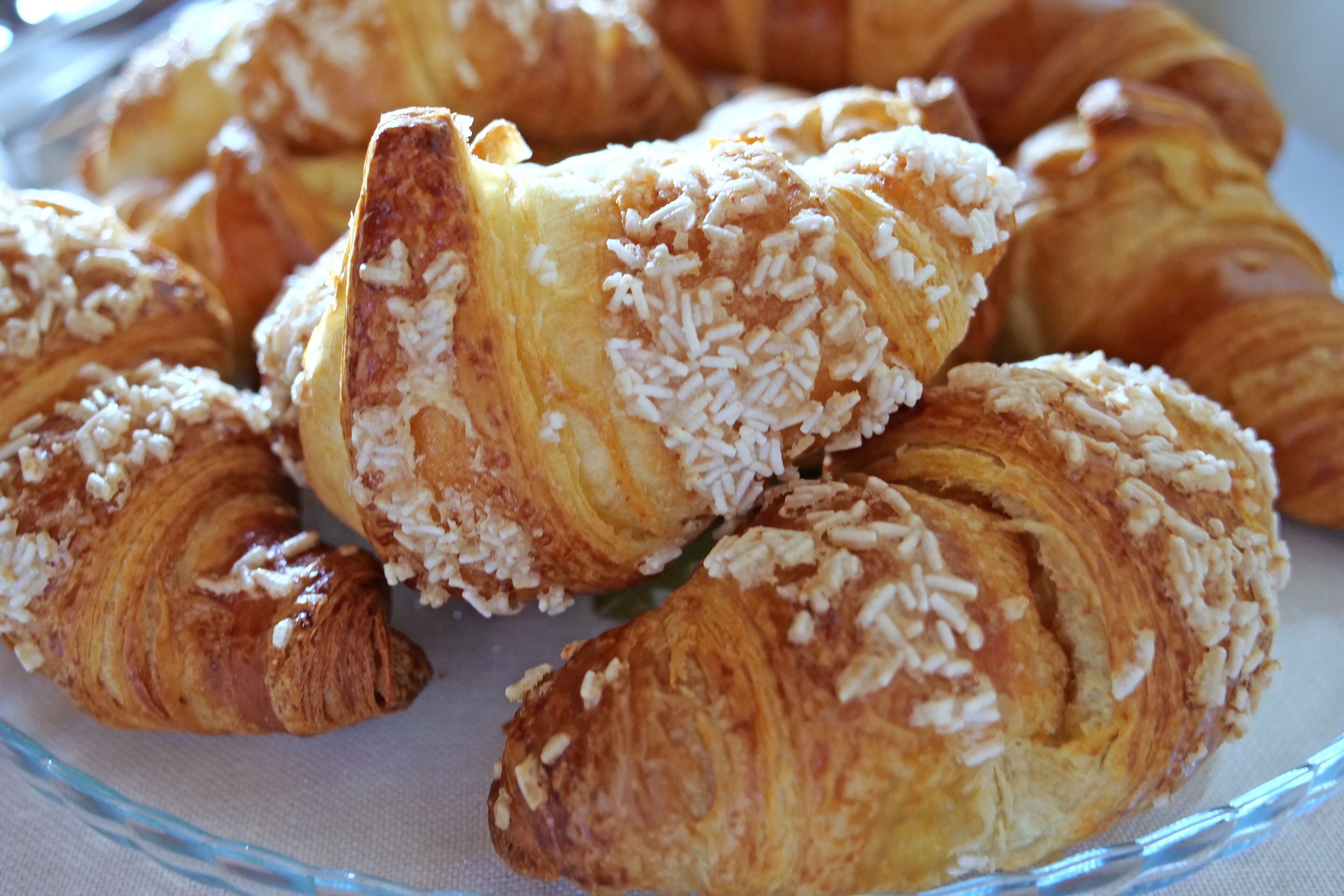 A glass plate with several croissants topped with white chocolate and coconut flakes.