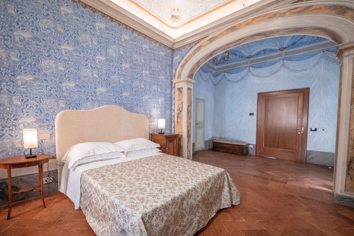 Une chambre à coucher avec un lit, des tables de chevet, une porte en bois et un sol carrelé.