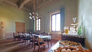 A dining area with wooden tables and chairs, a buffet with pastries, and a statue.