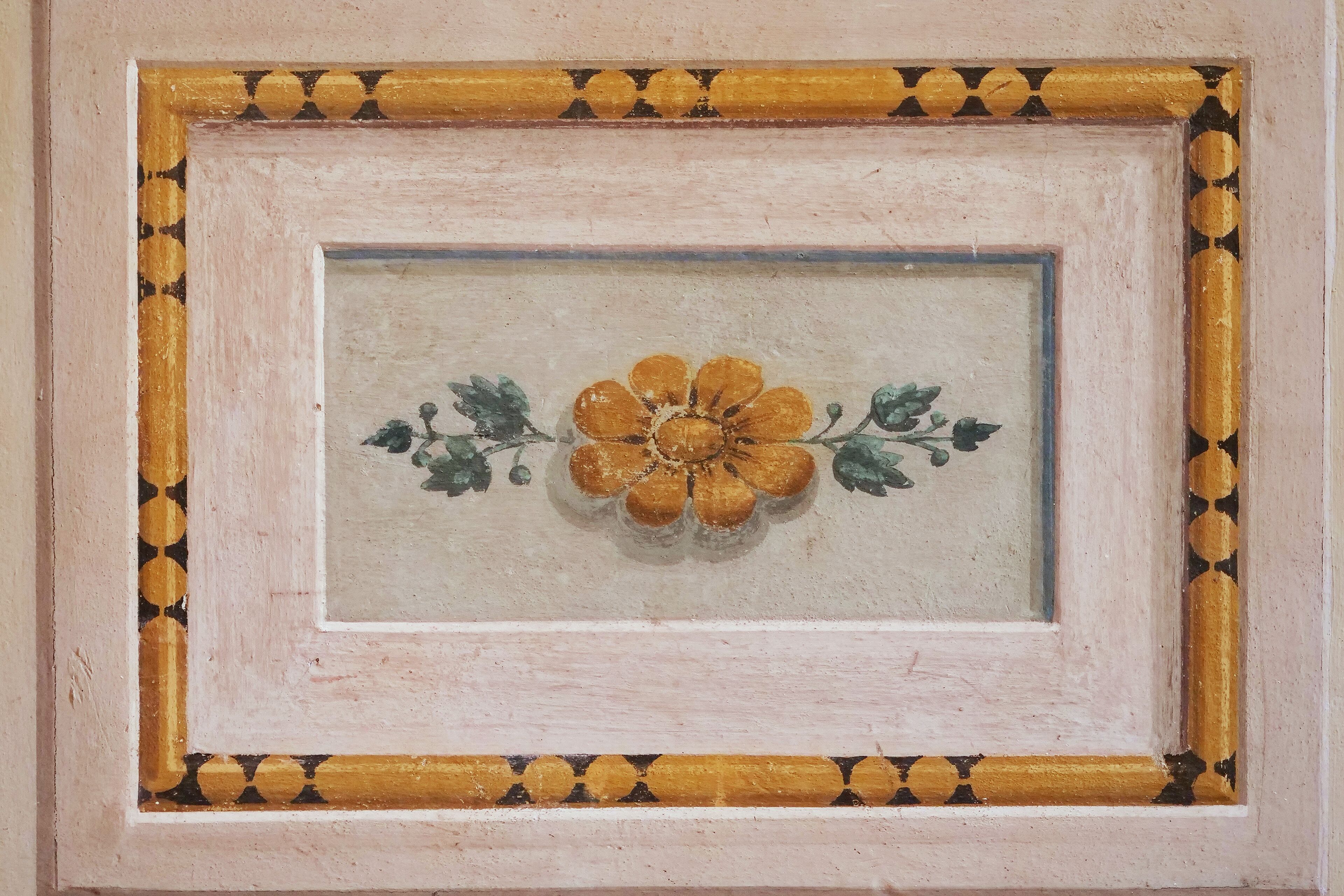 A framed artwork with a central flower design.