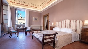 Un dormitorio con una cama grande, un escritorio, dos sillas y una ventana con vista a una torre de reloj.