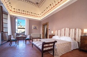 A bedroom with a large bed, a desk, two chairs, and a window with a view of a clock tower.