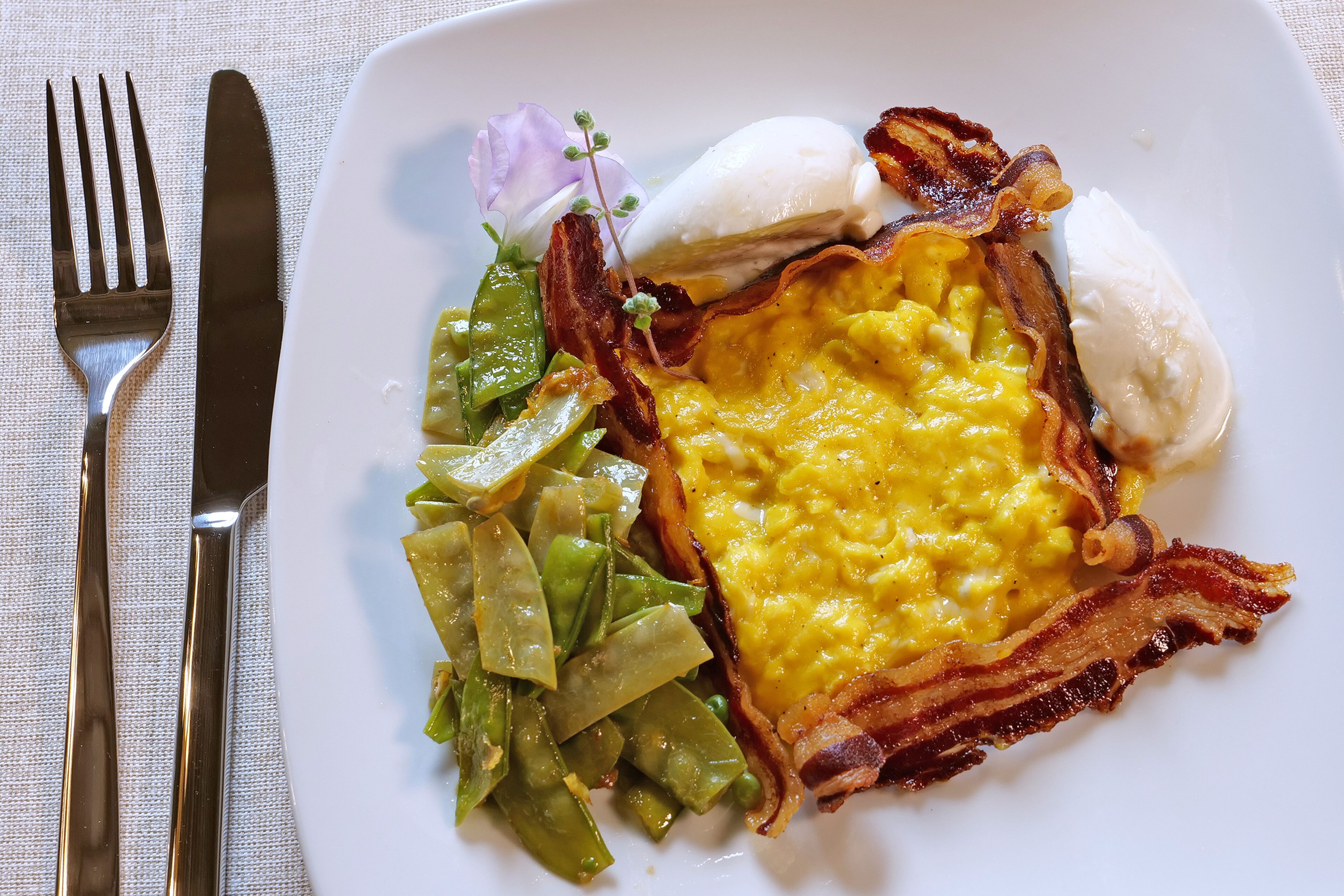 Une assiette contenant des œufs brouillés, du bacon et des haricots verts.